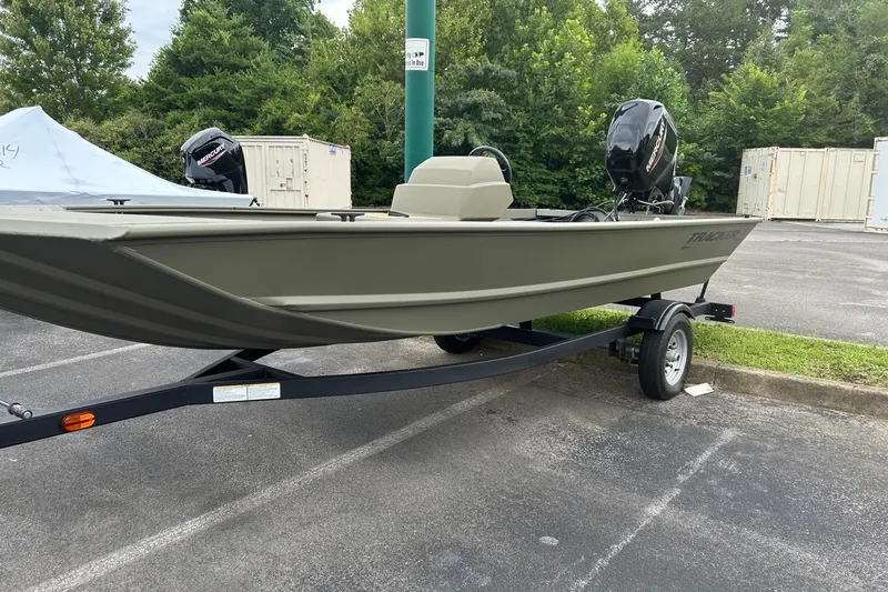 Slide: The Image of 2025 Tracker Grizzly 1648 SC boat on trailer, parked outdoors with trees in background. - 2