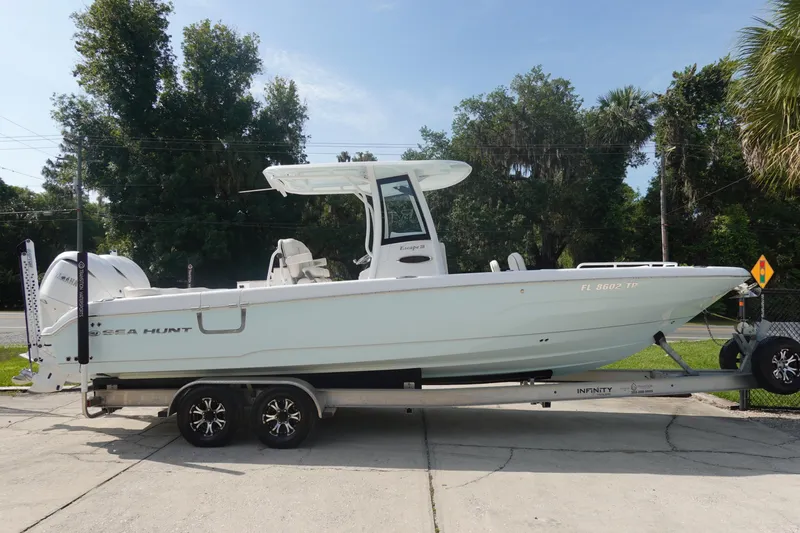 Slide: The Image of 2023 Sea Hunt Escape 28 boat on trailer, parked outdoors with trees in background. - 4