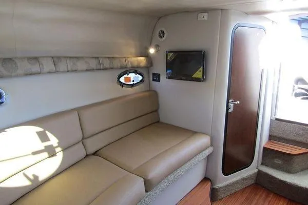 Slide: The Image of 2024 Crownline 310 CRX cabin interior with beige seating, TV, and wooden steps. - 10