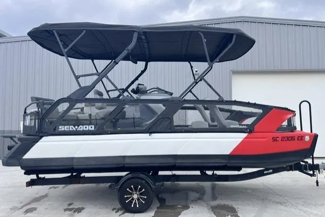 The Image of 2022 Seadoo Switch pontoon boat with canopy, parked on a trailer outside a warehouse. - 1