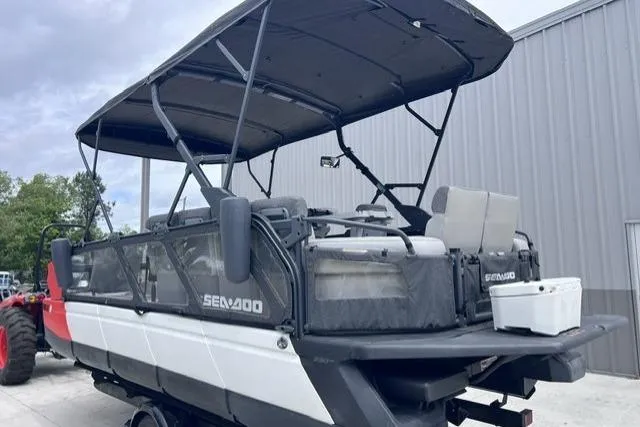Slide: The Image of 2022 Seadoo Switch pontoon boat with canopy, parked near a metal building. - 16