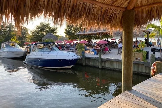 Slide: The Image of 2005 Rinker Fiesta Vee 320 docked near a lively waterfront restaurant with umbrellas. - 6