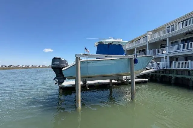 Slide: The Image of 2019 Cobia 280 Center Console boat docked on lift by waterfront homes. - 3
