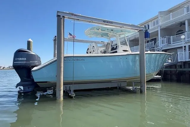 Slide: The Image of 2019 Cobia 280 Center Console boat on lift, docked near waterfront homes. - 4