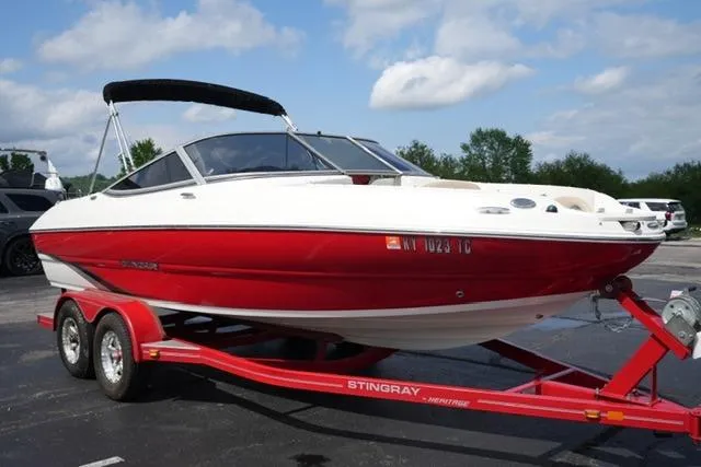 Slide: The Image of 2015 Stingray 208 LR boat on a red trailer, parked outdoors under a cloudy sky. - 10