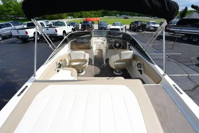 Slide: The Image of 2015 Stingray 208 LR boat interior with seating and steering wheel, parked outdoors. - 15