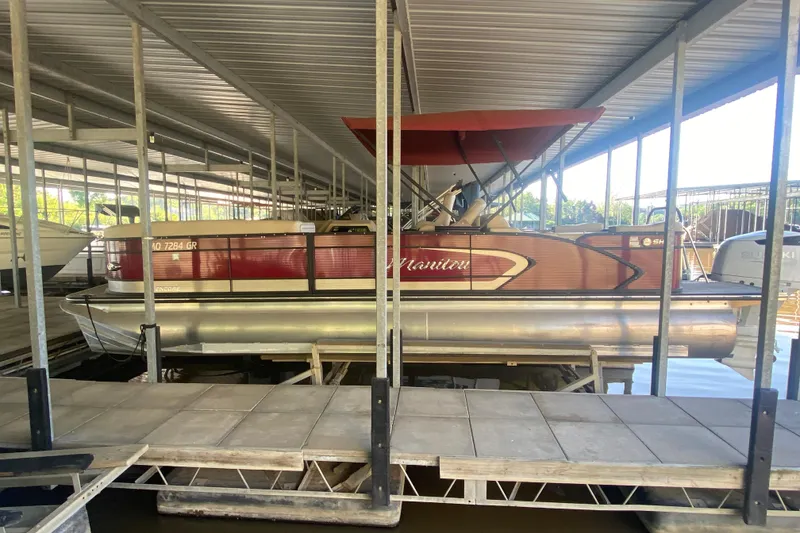 Slide: The Image of 2022 Manitou 25 Encore SR SHP pontoon boat docked under a covered marina. - 3