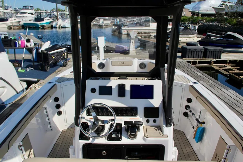Slide: The Image of 2024 Yamaha Boats 222 FSH Sport E dashboard at marina, showcasing controls and steering wheel. - 8