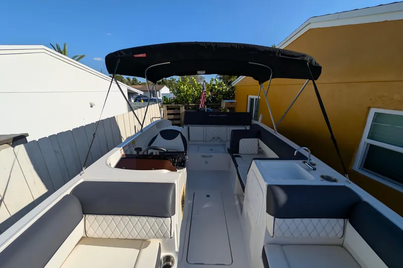 Slide: The Image of 2022 Bayliner DX 2000 boat with spacious seating and canopy, docked near a yellow house. - 12