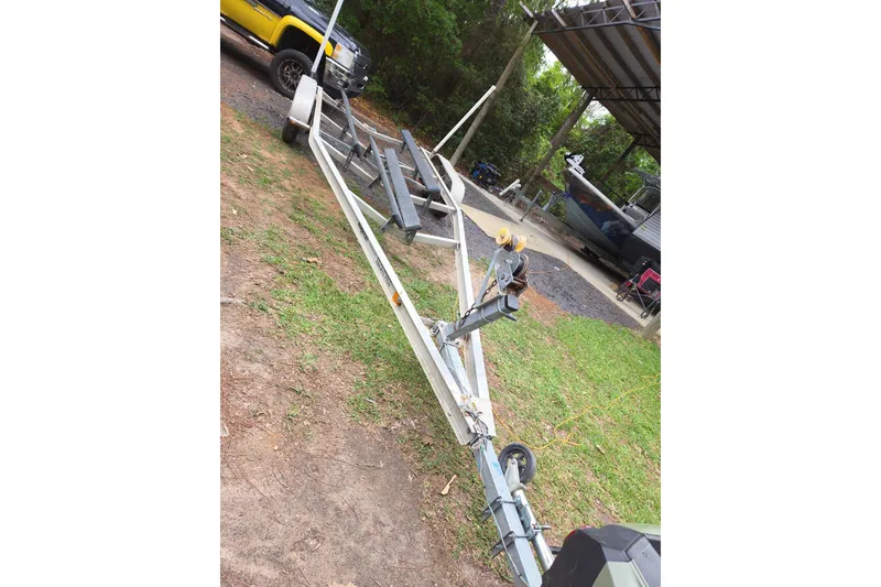 Slide: The Image of Boat trailer parked on grass beside a yellow truck, near a covered boat area. - 13