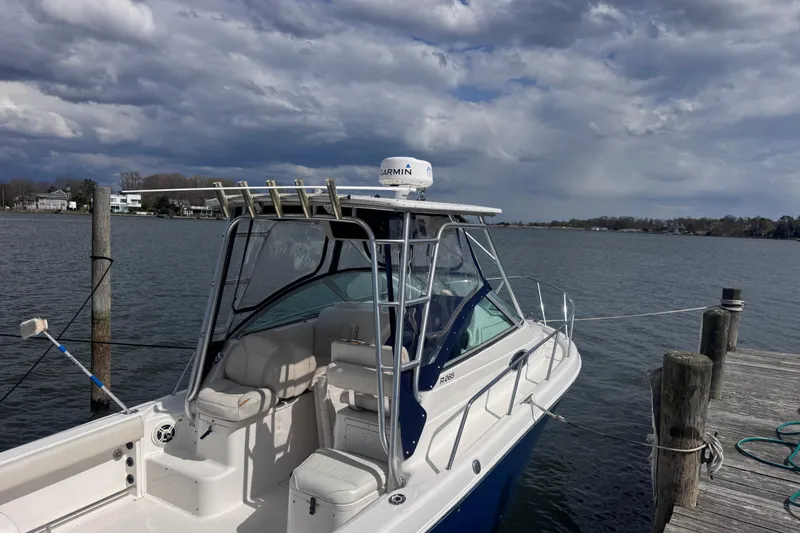 Slide: The Image of 2003 Robalo R265 Walkaround boat docked by a scenic waterfront under cloudy skies. - 2