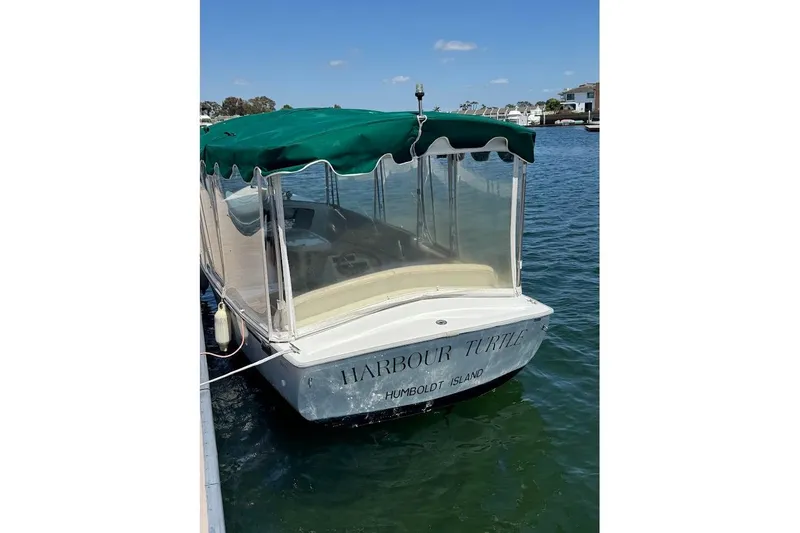 Slide: The Image of Electric boat "Harbour Turtle" docked, featuring green canopy, clear sides, and calm water backdrop. - 6