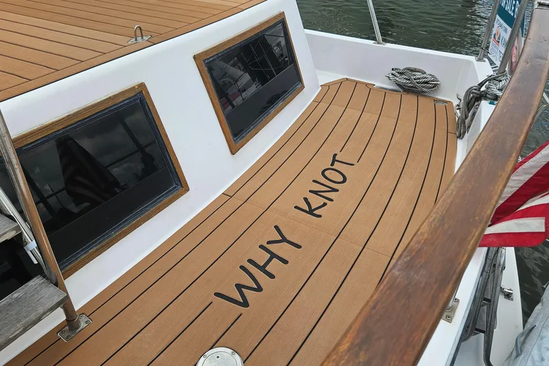 Slide: The Image of 1988 Overseas Monk 42 boat deck with "WHY KNOT" text, featuring wooden accents and American flag. - 94