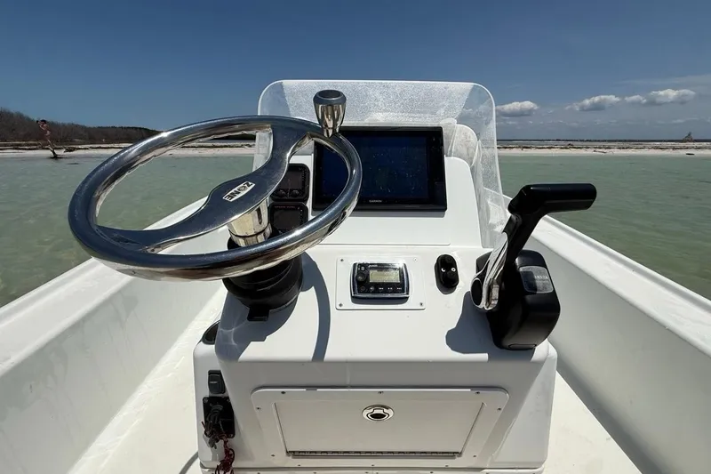 Slide: The Image of 2013 Yellowfin 21 Bay boat dashboard with steering wheel and controls, set against a coastal backdrop. - 14