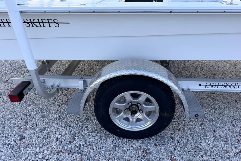 Slide: The Image of 2019 Mitzi Skiffs 17 boat trailer with aluminum fender and wheel on gravel surface. - 17