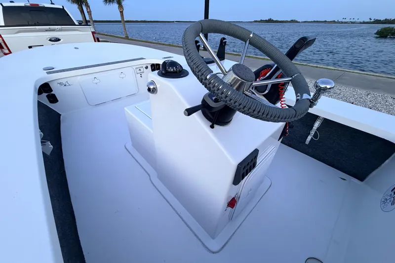 Slide: The Image of 2019 Mitzi Skiffs 17 boat interior with steering wheel, docked by a scenic waterfront. - 38