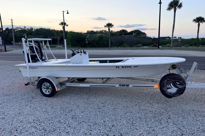 Slide: The Image of 2019 Mitzi Skiffs 17 boat on trailer, parked on gravel, with palm trees in background. - 6