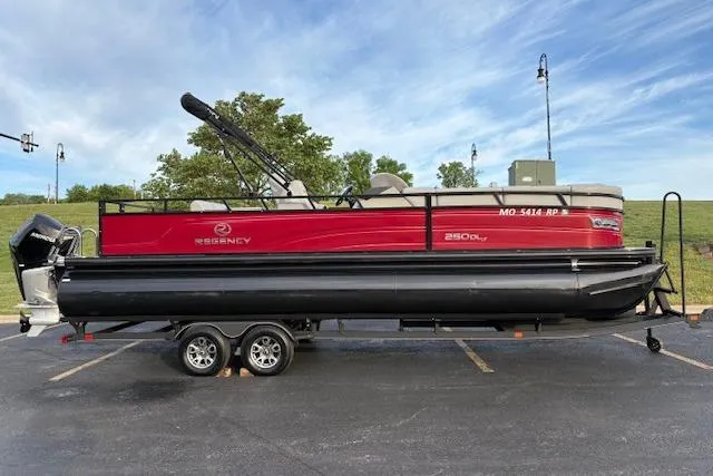 The Image of 2024 Regency 250 DL3 pontoon boat on trailer, red and black design, parked outdoors. - 1