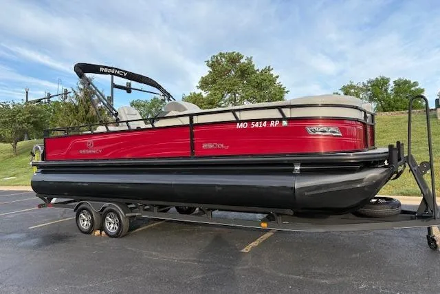 Slide: The Image of 2024 Regency 250 DL3 pontoon boat on trailer, red and black design, parked outdoors. - 3