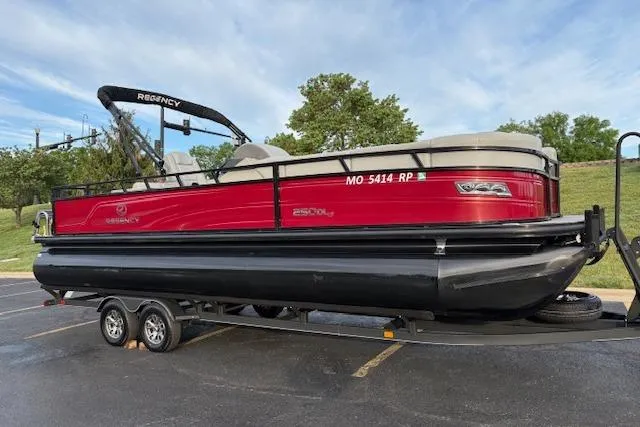 Slide: The Image of 2024 Regency 250 DL3 pontoon boat on trailer, red and black design, parked outdoors. - 4