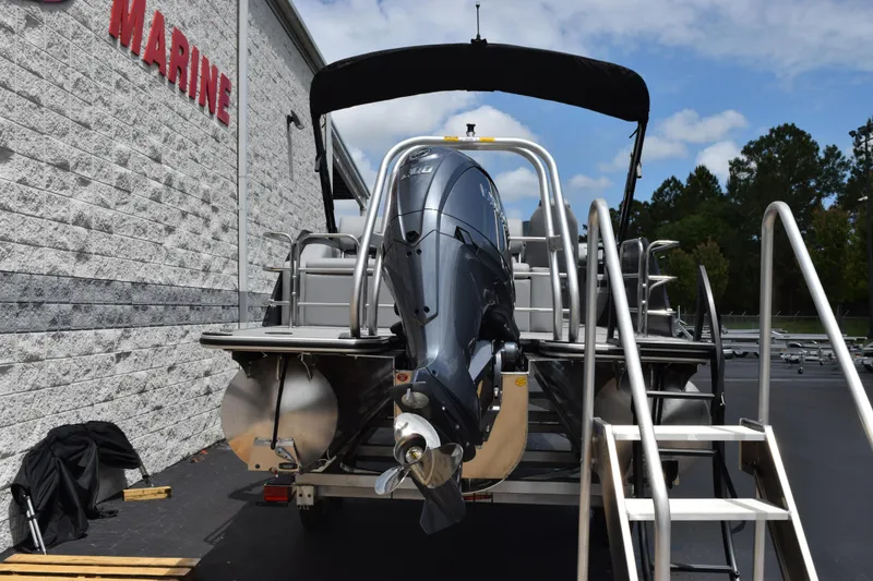 Slide: The Image of 2026 Bentley Pontoons Legacy 243 Swingback with outboard motor, parked near a marine building. - 5