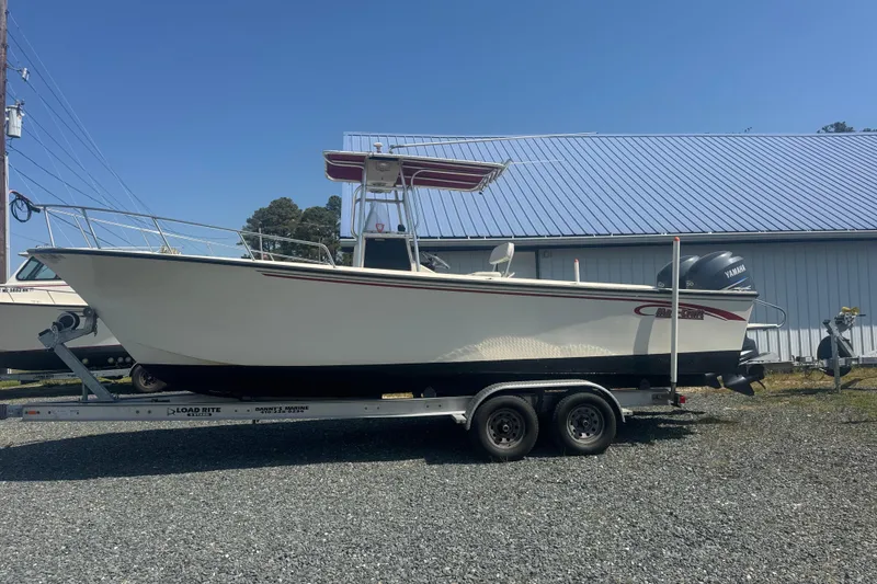 The Image of 1999 May-Craft 2500 boat on trailer, parked outdoors under clear blue sky. - 0