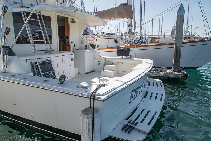 Slide: The Image of 1989 Bertram 50 Convertible yacht docked at marina, featuring spacious deck and fishing equipment. - 5