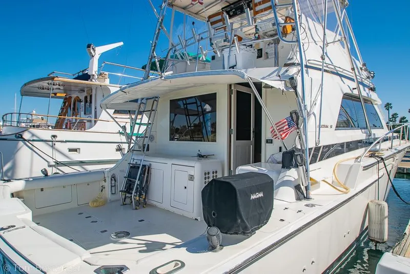 Slide: The Image of 1989 Bertram 50 Convertible yacht docked at marina, featuring spacious deck and American flag. - 6