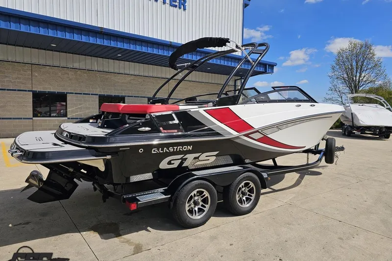 Slide: The Image of 2020 Glastron GTS 225 boat on trailer, parked outside a building under a clear sky. - 12