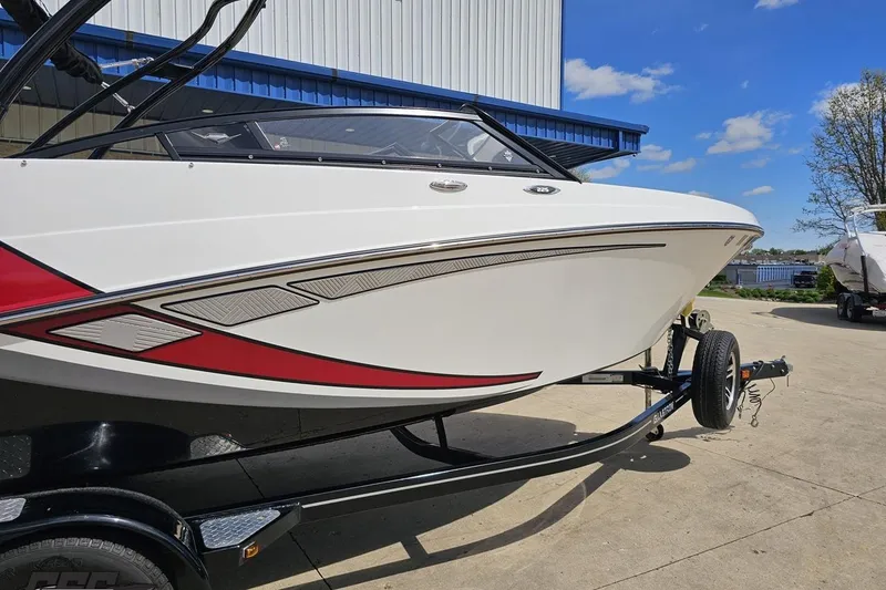 Slide: The Image of 2020 Glastron GTS 225 boat on trailer, white with red accents, parked outdoors. - 13