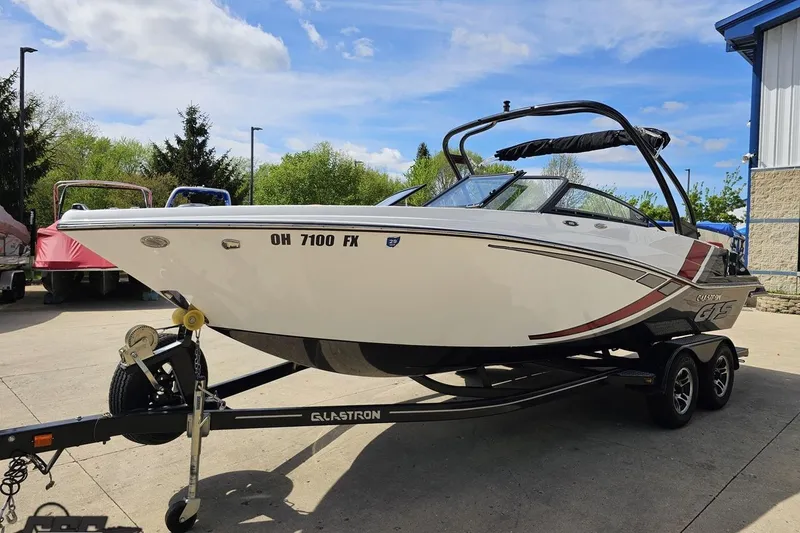 Slide: The Image of 2020 Glastron GTS 225 boat on trailer, parked outdoors under a clear sky. - 21
