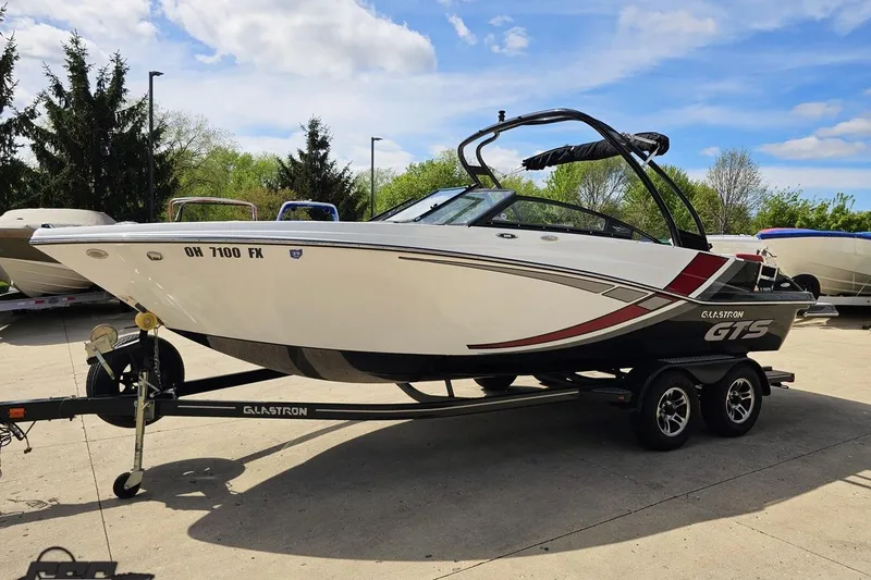Slide: The Image of 2020 Glastron GTS 225 boat on trailer, parked outdoors under a blue sky. - 22