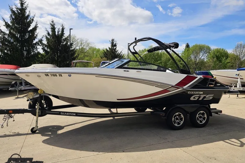 Slide: The Image of 2020 Glastron GTS 225 boat on trailer, parked outdoors under a blue sky. - 23