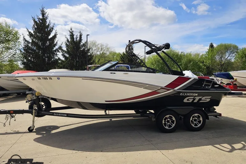 Slide: The Image of 2020 Glastron GTS 225 boat on trailer, parked outdoors under a blue sky. - 24