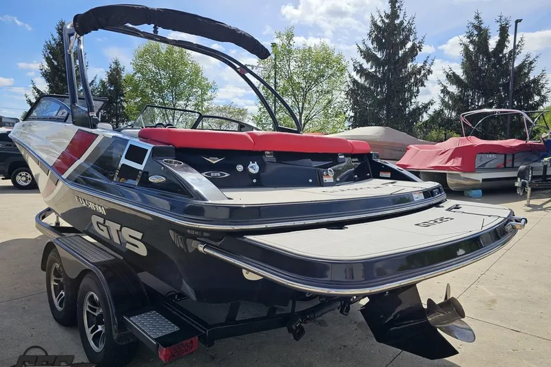 Slide: The Image of 2020 Glastron GTS 225 boat on trailer, parked outdoors with trees in background. - 32