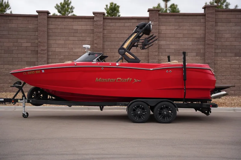 The Image of 2022 MasterCraft XStar S boat in vibrant red on a trailer, parked by a brick wall. - 1