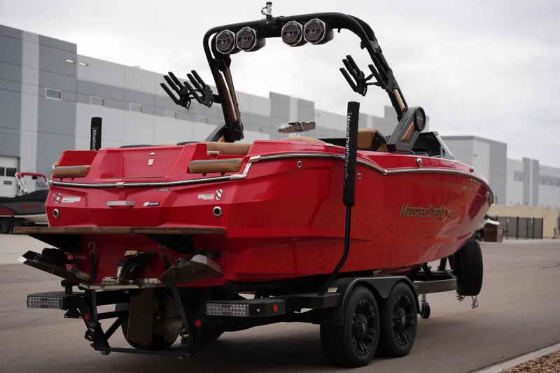 Slide: The Image of Red 2022 MasterCraft XStar S boat on trailer, parked near industrial buildings. - 4