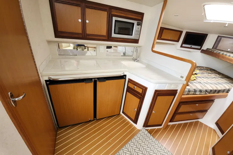 Slide: The Image of 2009 Cabo 36 Express yacht interior with kitchenette, featuring wood cabinetry, microwave, and compact fridge. - 16
