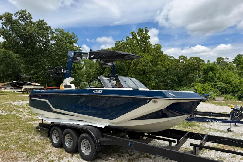 Slide: The Image of 2026 Nautique Super Air Nautique GS24 boat on trailer, parked outdoors with trees in background. - 2