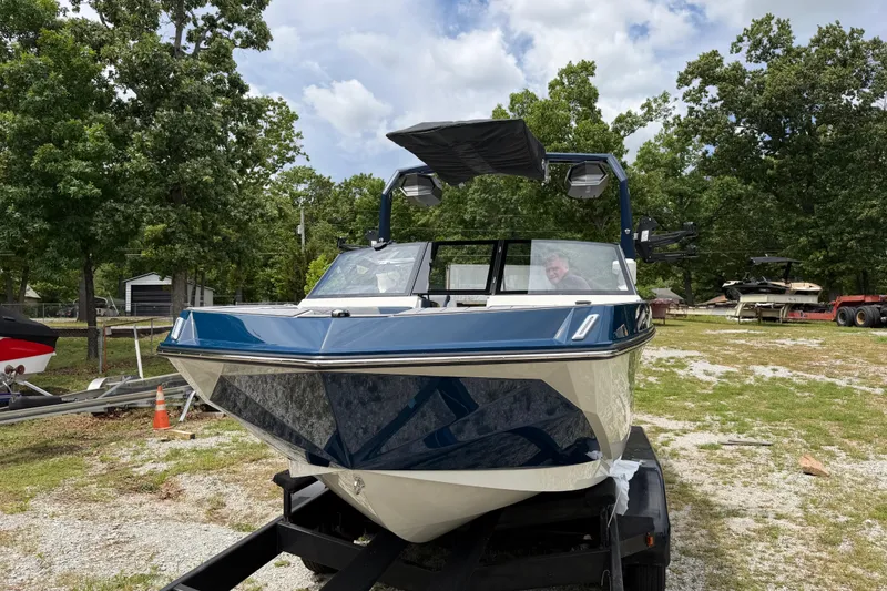 Slide: The Image of 2026 Nautique Super Air Nautique GS24 boat on trailer, surrounded by trees and equipment. - 5