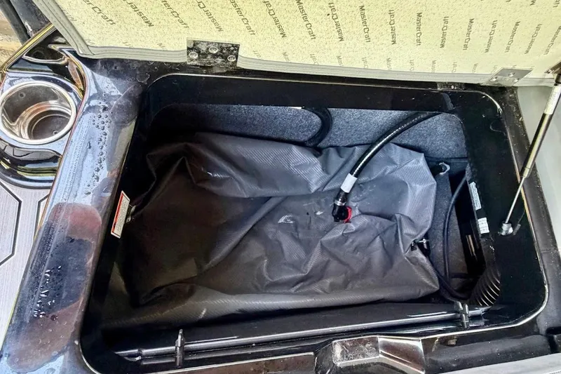 Slide: The Image of Open storage compartment in 2023 MasterCraft NXT20 boat, featuring a black bag and hose. - 21