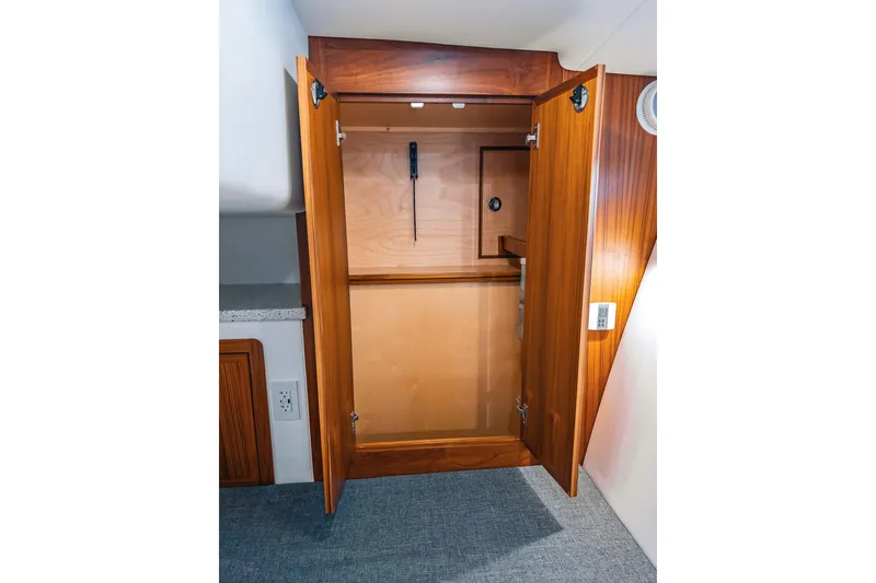 Slide: The Image of Wooden closet interior on a 2024 Lindell 46 boat, featuring open doors and a hanging rod. - 57