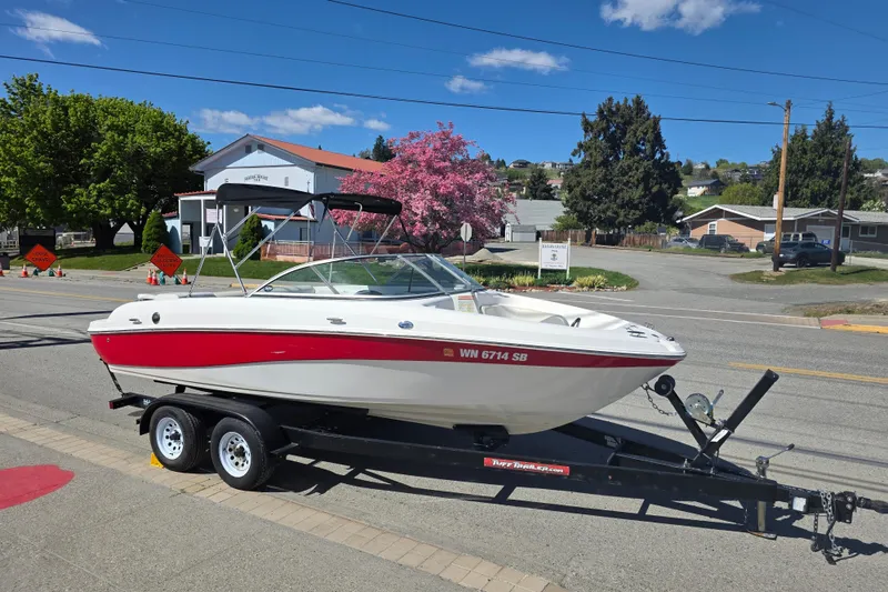 The Image of 2014 Reinell 207 LS boat on trailer, parked on street with trees and houses in background. - 0
