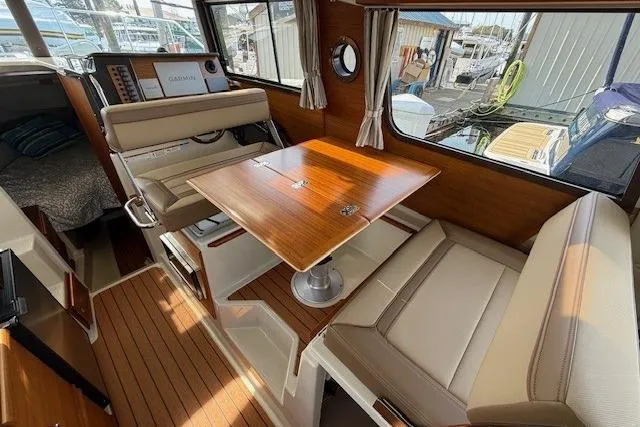 Slide: The Image of 2023 Ranger Tugs R-27 interior with wood table, beige seating, and large windows. - 10