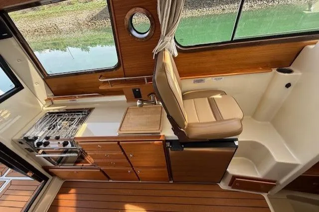 Slide: The Image of 2023 Ranger Tugs R-27 interior with kitchen, stove, and seating, featuring wood accents and window view. - 11