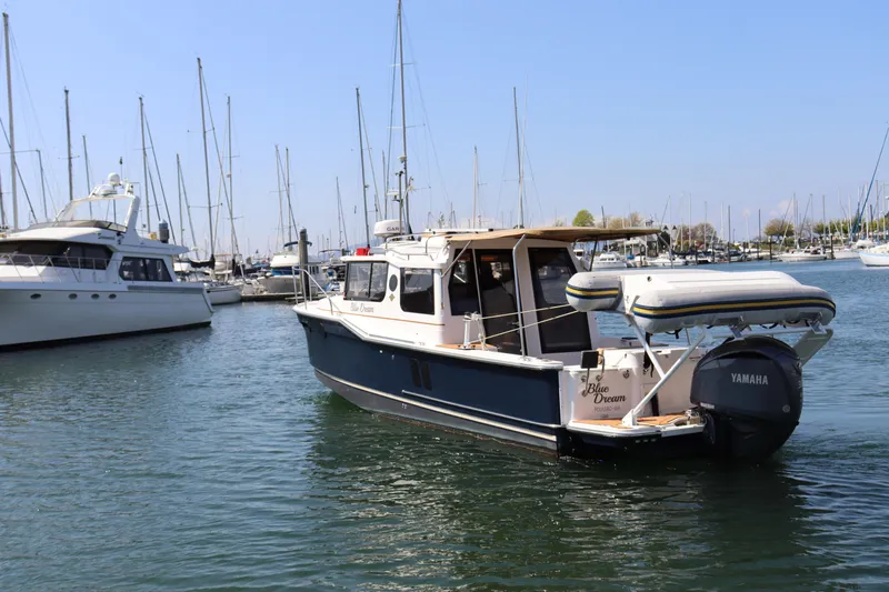 Slide: The Image of 2023 Ranger Tugs R-27 boat docked in a marina with sailboats in the background. - 2