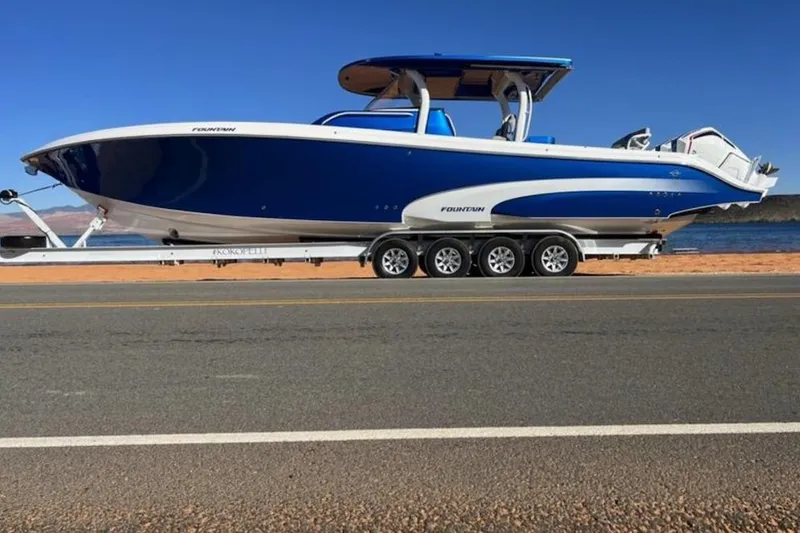 The Image of 2023 Fountain 43 NX boat on trailer by the water, showcasing sleek blue design. - 1
