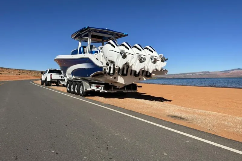 Slide: The Image of 2023 Fountain 43 NX boat on trailer by lakeside road under clear blue sky. - 4