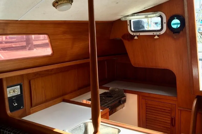 Slide: The Image of 1986 Farr 1020 yacht interior with wooden cabinetry and compact kitchen area. - 5