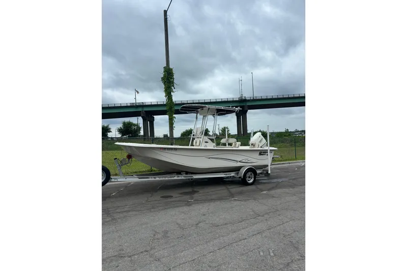 The Image of 2019 Carolina Skiff 218 DLV boat on trailer, parked near highway under cloudy sky. - 1
